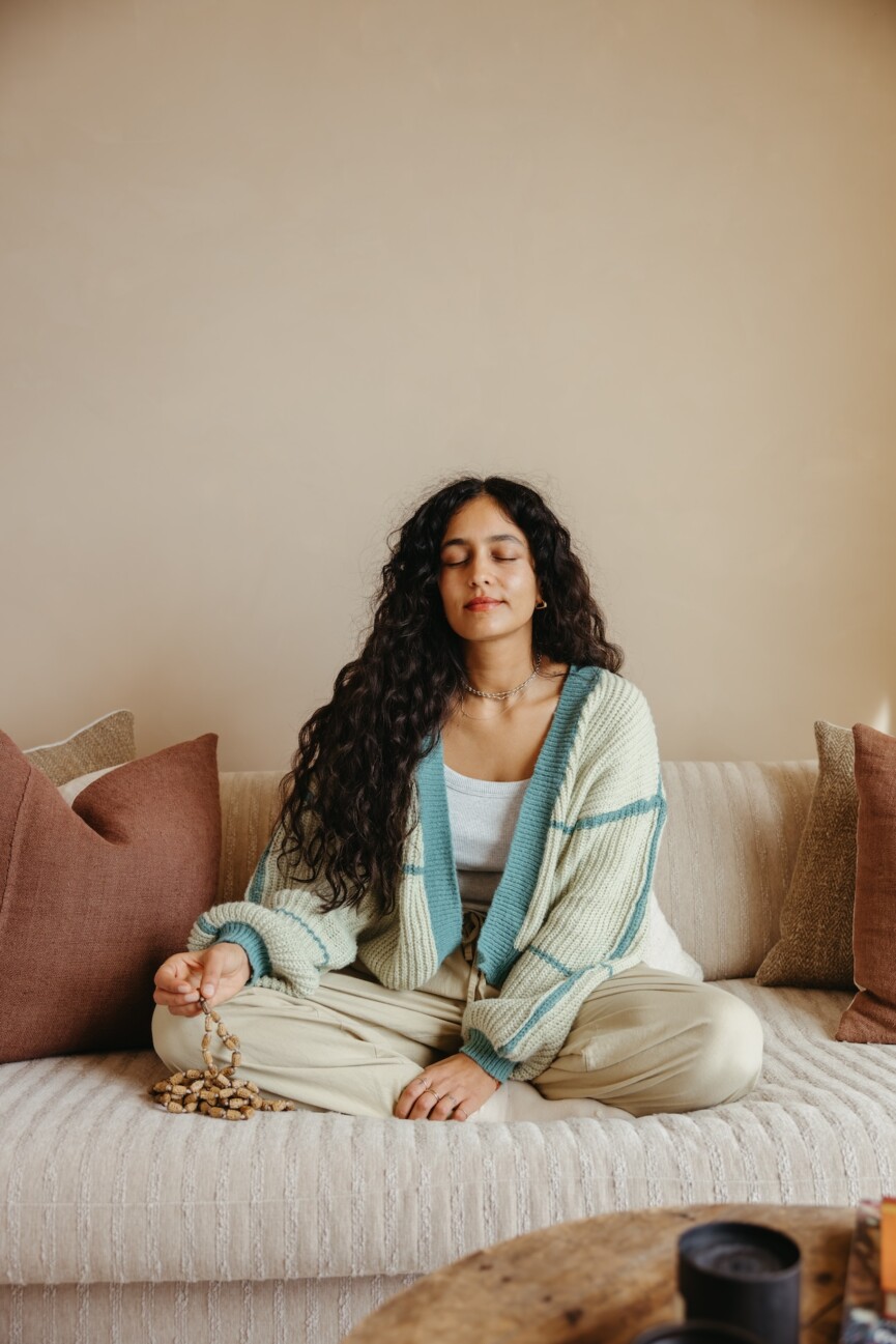 A woman sitting on a couch cross-legged with her eyes closed. 